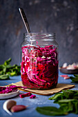 A jar of pickled red cabbage with a fork in it, photographed against a dark background