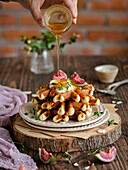 Waffelstapel mit Feigen, Sahne und Thymian mit flüssigem Honig, auf einem rustikalen Holzbrett
