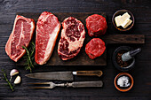Various raw Black Angus prime steaks Blade on bone, striploin, rib eye, tenderloin filet mignon on wooden board and spices