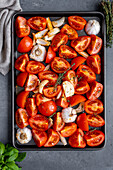 Tomato slices, onion slices and garlic halves on a baking sheet to be roasted.