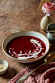 A bowl of beetroot soup with cream and almond flakes on a wooden table