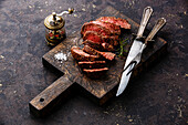 Sliced grilled roast beef steak with knife and fork on a wooden cutting board