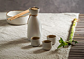 Japanisches Sake-Stillleben mit einem Bambuszweig, heller Leinenhintergrund, asiatische Zeremonie