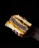 Anonymous person holding a piece of appetising fried sandwich with patty and mustard on a black background