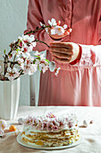 crepe cake or blini cake for Easter party, rose pink background, almond flowers, rose pink background, woman hands