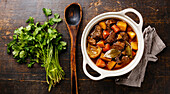 Braised beef with potatoes, carrots and spices in a ceramic pot on a wooden background