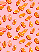 Composition of orange-coloured vitamin pills on a pink background in a bright studio, top view