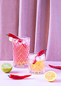 Transparent glasses filled with refreshing and cold cocktails served with pepper and ice cubes placed on the table with lemon and lime