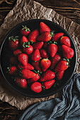 Black bowl of fresh strawberries on crumpled paper, with green napkin, over a wooden table