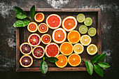 Citrus fruits (orange, blood orange, grapefruit, lemon, lime) cut in half and arranged by color in rustic wood box with fresh citrues leaves