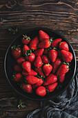 Black bowl with fresh strawberries, with green napkin, on a wooden table