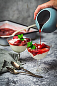 Joghurt und geröstete Erdbeerparfaits in alten Gläsern mit Sirup aus einem blassblauen Krug