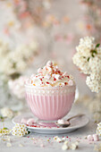 A glass cup with pink hot chocolate drink topped with whipped cream and mini marshmallows.