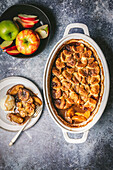 Apple cobbler in a ceramic baking dish, served on a plate with vanilla ice cream and a bowl of fresh apples