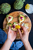Women's hands rub a slice of raw artichoke with a slice of lemon
