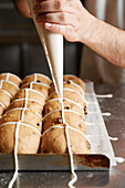 Baker spraying a cross" on raw fruit buns baked with yeast and sourdough"