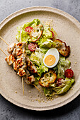 Caesar salad with chicken breast on a skewer and egg on a plate