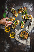 Male hand choosing a Mushroom and goat cheese crostini arranged on a pewter plate, with sherry in glasses, mushrooms in small dish