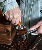 Barista holding portafilter and coffee tamper making coffee in coffee shop or café, dark backgrounds