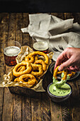 Battered Onion Rings on metal basket with herb dipping sauce and beer glasses