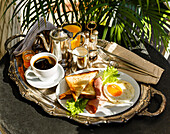 Frühstück mit Spiegelei, Schinken, Toast und Kaffee auf einem runden Tisch an einem sonnigen Sommermorgen