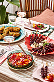 Ein Picknick mit Salat an einem Tisch im Freien, mit frischem Obst und Gebratenem, auf einem gestreiften Tischtuch
