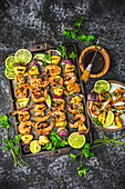 Skewers of grilled shrimp, pineapple and red onion on a baking tray and plate with glaze in bowl