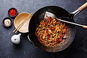 Udon stir-fry noodles with chicken and vegetables in wok pan on dark stone background