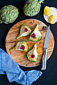 An artichoke quartered on a wooden board, a knife, lemon slices and whole artichokes accompany.