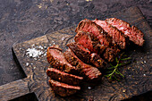 In Scheiben geschnittenes gegrilltes Steak mit Roastbeef und Rosmarin auf einem Holzschneidebrett