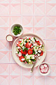 Spring salad with strawberries, cucumber, radish and parsley on pink tiles