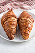 Two croissants on a white plate against a red striped kitchen towel