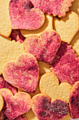 Ausgestanzte Herzkekse mit rosafarbenem Zucker auf einem rosafarbenen Marmorhintergrund