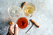 View from above of an unrecognisable person presenting three main types of dry Georgian wines - white, red and amber - on a grey concrete table with corkscrew and corks