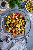 Green olive salad with onions, cherry tomatoes, parsley and dill in a glass bowl