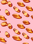 Composition of orange vitamin pills on a pink background in a bright studio viewed from above