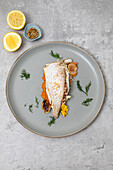 Freshly baked market fish served with fresh vegetables on a grey plate