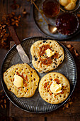 A pikelet, fruit pikelet and a crumpet on a plate with a knob of butter on the top of each one.,