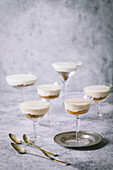 Arrangement of vanilla parfaits with biscuit crumbs in vintage cocktail glasses on grey background and small silver plate