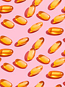 Composition of orange vitamin pills on a pink background in a bright studio seen from above