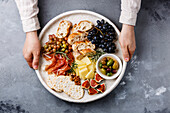 Italienische Snacks Essen mit Schinken, Oliven, Käse, getrocknete Tomaten, Wurst und Brot in männlichen Händen auf konkreten Hintergrund