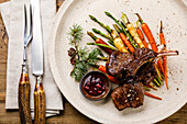 Grilled Venison Ribs with baked vegetables and berry sauce on wooden background