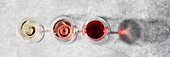 Flat-lay of red, rose and white wine in glasses on grey stone background. Wine bar, winery, wine degustation concept. Minimalistic trendy photography.