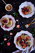 Englisches Gebäck (Crumpets) mit Beeren und Honig auf schwarzem Marmorboden, Flatlay