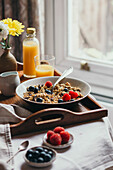 Breakfast tray with muesli, berries and juice next to a window