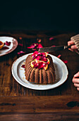 Blood orange cake on a plate against a wooden table, being sliced by a woman with a knife