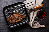 Gegrilltes Steak Striploin in gusseiserner Pfanne und Rotwein auf schwarz verbranntem Holzhintergrund