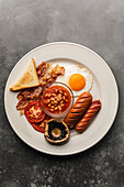 Full fry up English breakfast with fried eggs, sausages, bacon, beans, toasts
