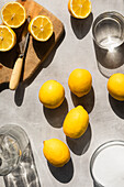 Zitronen in hartem Licht, mit Zucker, Wasser und geschnittenen Zitronen umgeben