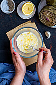 Women's hands making an artichoke dipping sauce in a small bowl